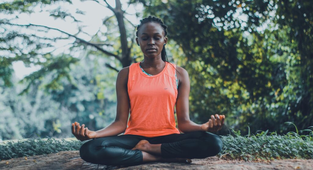 pexels-photo-2908175-2908175 A woman meditating peacefully outdoors in a lush green setting, promoting relaxation and mindfulness.