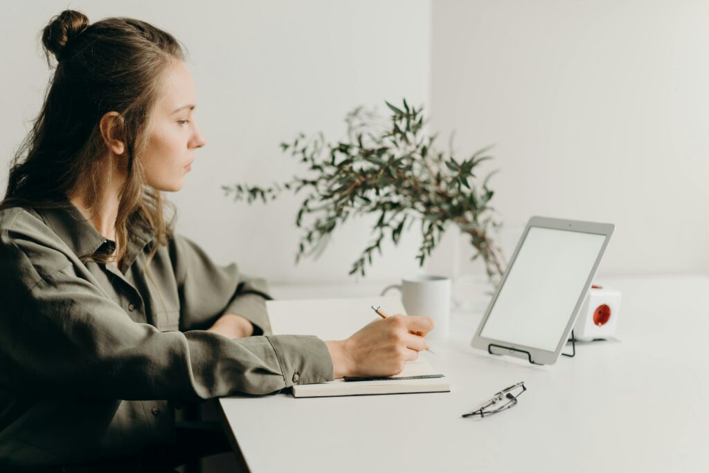 pexels-photo-4065891-4065891 Freelancer writing notes in a minimalist home office with a white tablet, plant, and reading glasses.