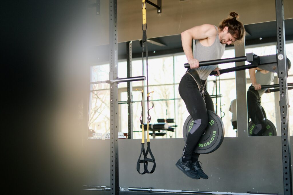 Fit man performing weighted pull-ups in a gym setting, showing strength and determination.