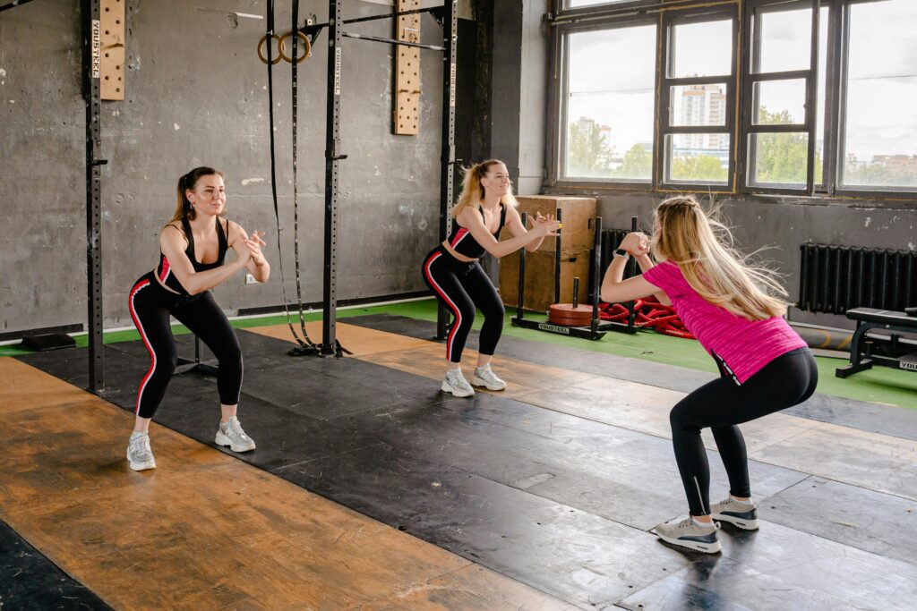 A group of women exercising inside a gym, performing squats in sportswear.