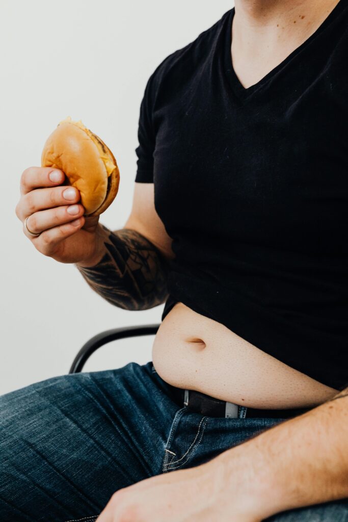 pexels-photo-5714274-5714274 Man wearing black shirt sits holding a burger, highlighting casual eating habits.