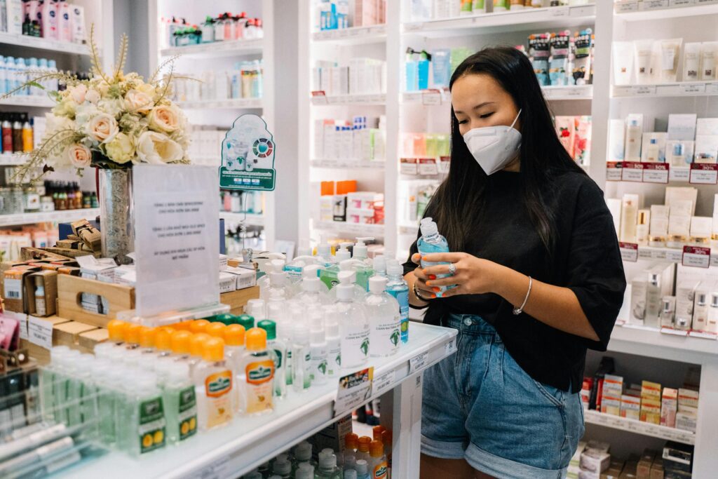 Asian woman selecting hand sanitizer in a well-stocked pharmacy, emphasizing health and hygiene.