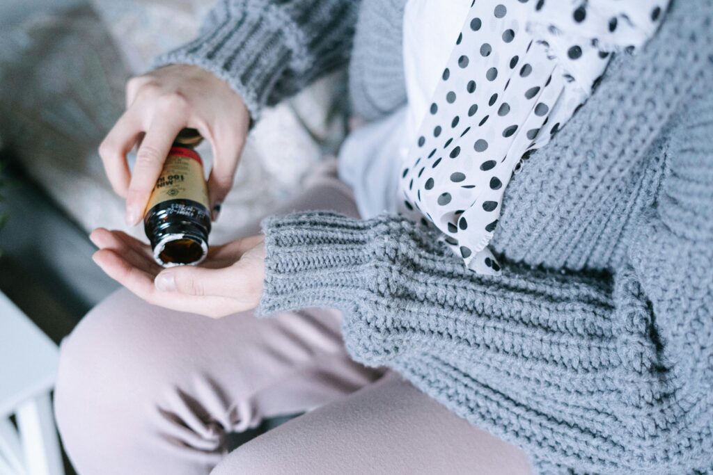 pexels-photo-6436284-6436284 Close-up of a woman in cozy clothing holding a medicine bottle in her hands.