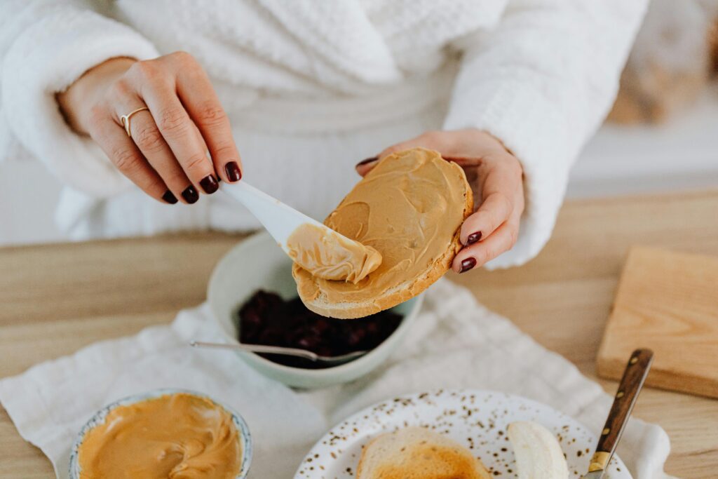 pexels-photo-6659874-6659874 Close-up of a woman spreading creamy peanut butter on toast, perfect for breakfast.