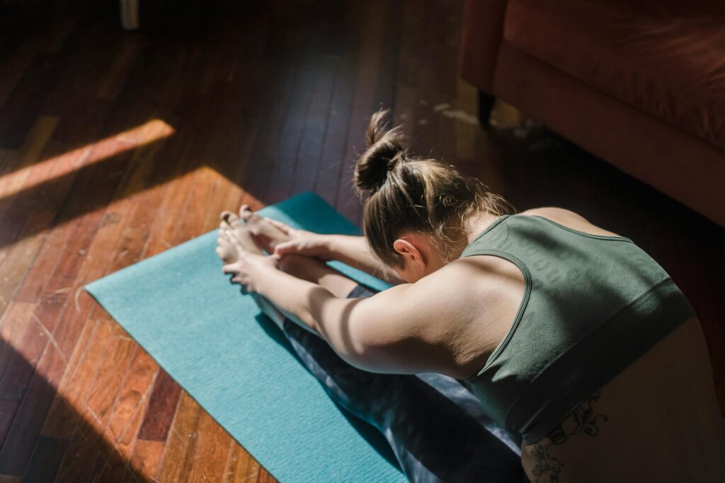 pexels-photo-6697123-6697123 A woman stretches in a yoga pose on a mat in a sunlit room, emphasizing relaxation.