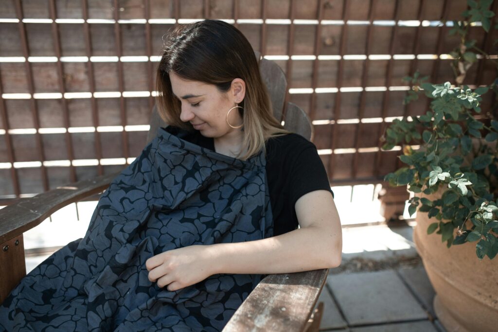 pexels-photo-6849481-6849481 Mother sitting outdoors comfortably breastfeeding her baby under a stylish nursing cover.