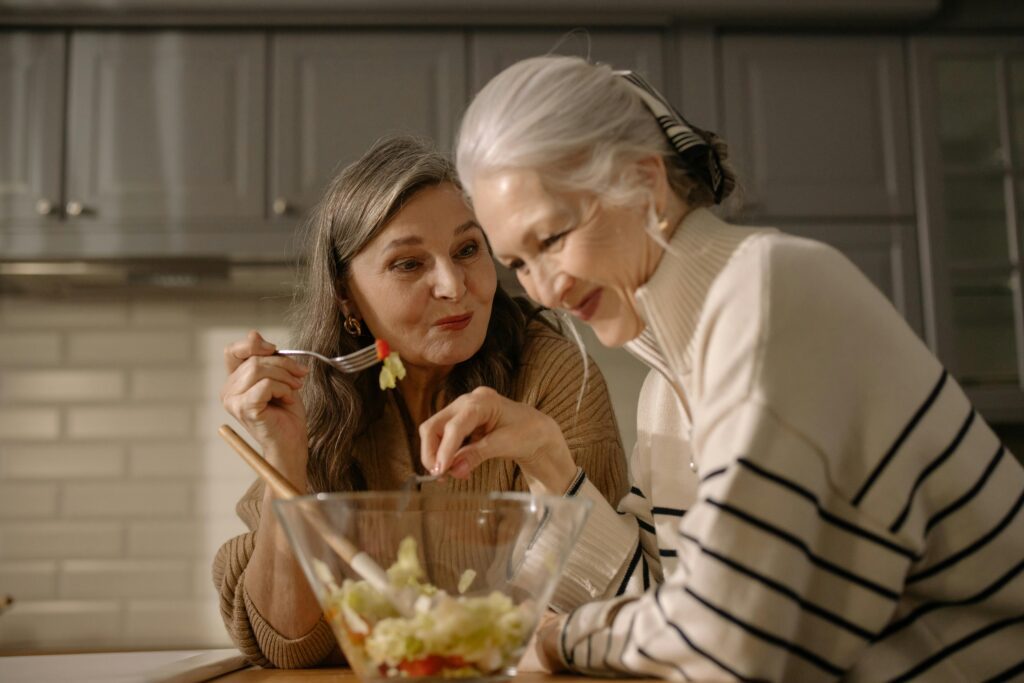 pexels-photo-6928667-6928667 Two senior women smiling and enjoying a fresh salad in a cozy kitchen setting.