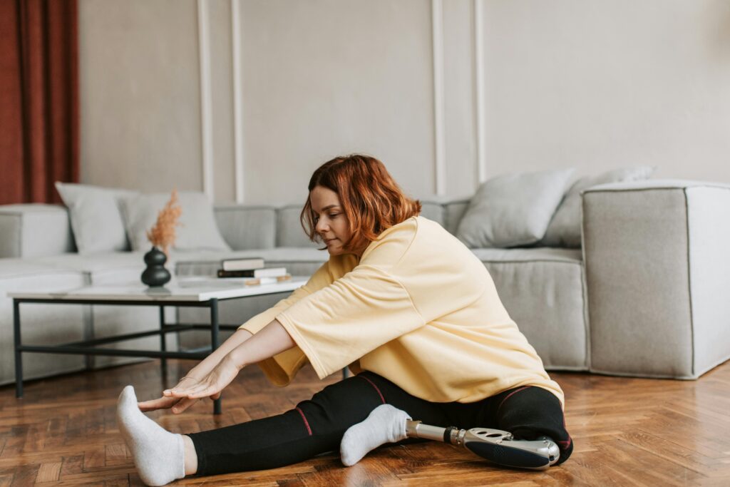 pexels-photo-7153950-7153950 A woman with a prosthetic leg stretches on a wooden floor in her living room, embracing fitness.