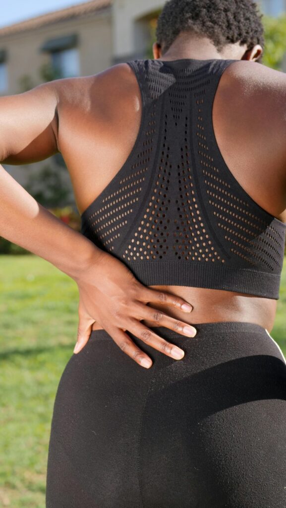 pexels-photo-7298685-7298685 A woman in sportswear gripping her lower back, potentially indicating discomfort, set in an outdoor environment.