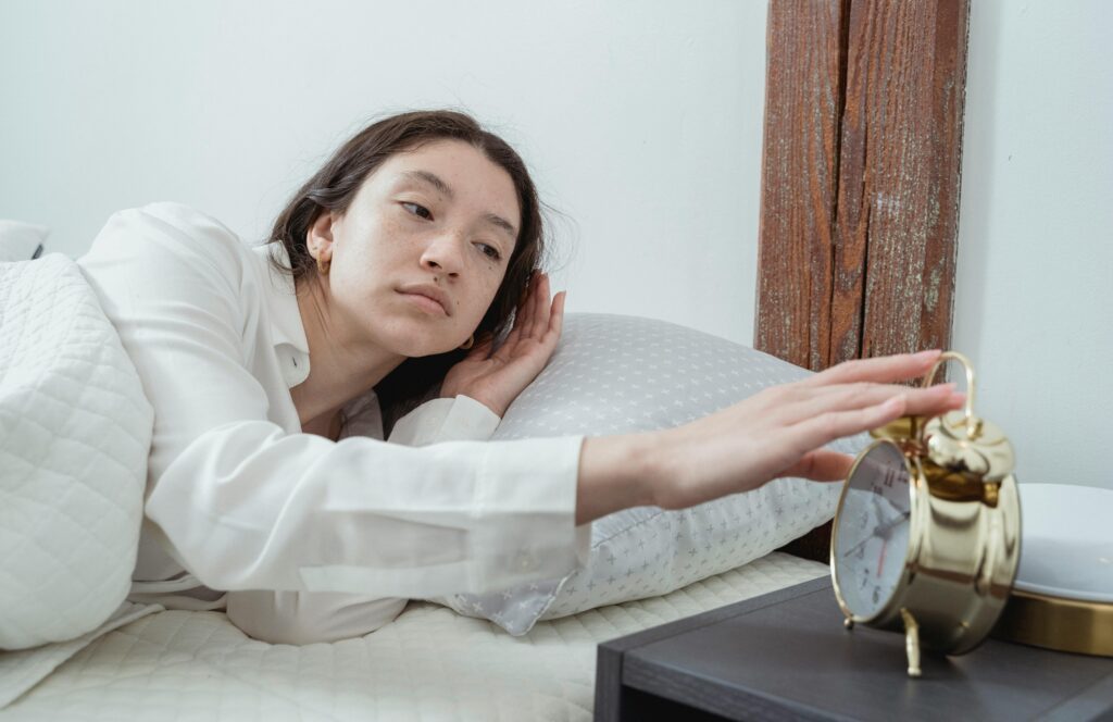 pexels-photo-7622504-7622504 Sleepy young brunette female in white sleepwear resting in comfortable bed and waking up with alarm clock at home in morning time