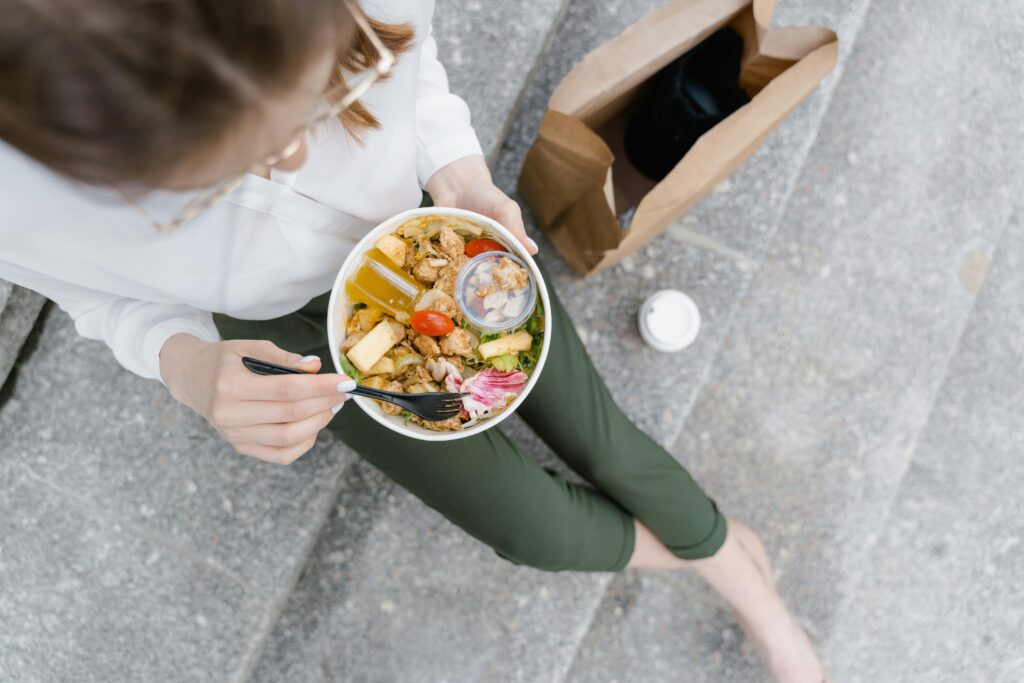 Top-down view of a woman enjoying a healthy salad outdoors during a casual lunch break.