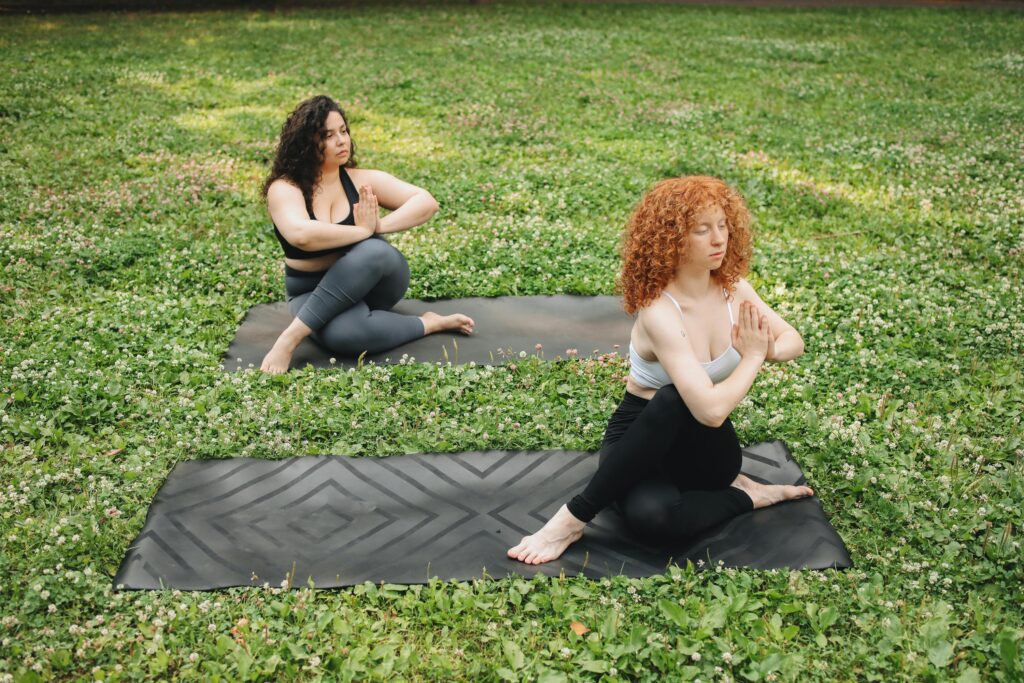 Two women practicing yoga in a tranquil outdoor setting, surrounded by lush grass.