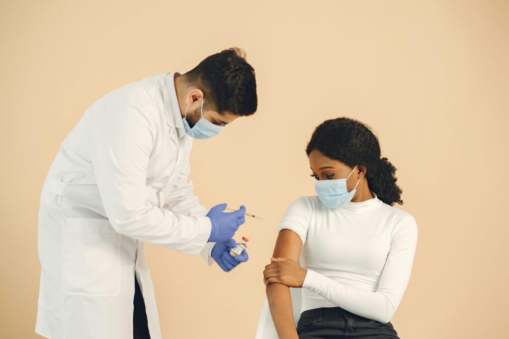 A doctor gives a vaccine shot to a woman wearing a mask in a studio setting.