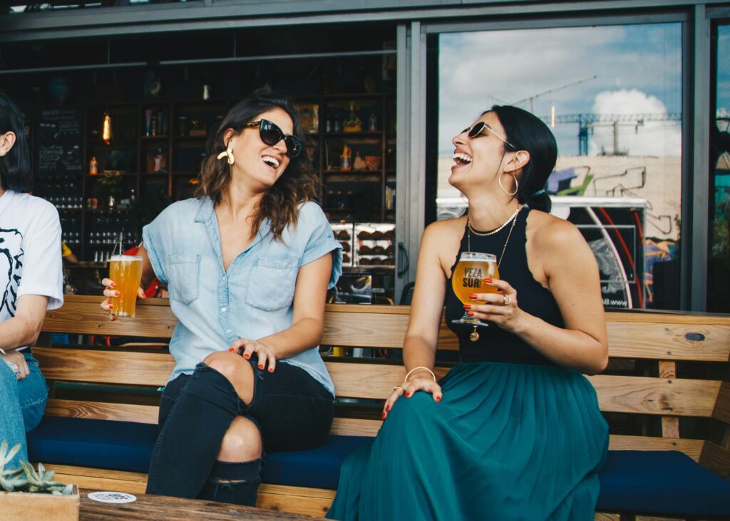 pexels-photo-1267696-1267696-1 Two women laughing and enjoying drinks outdoors at a trendy bar, creating a vibrant and social atmosphere.