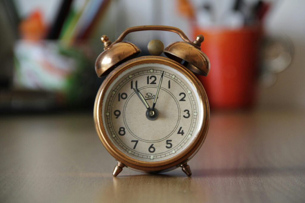 pexels-photo-210528-210528 A vintage copper alarm clock with bells placed on a desk with blurred objects in the background.