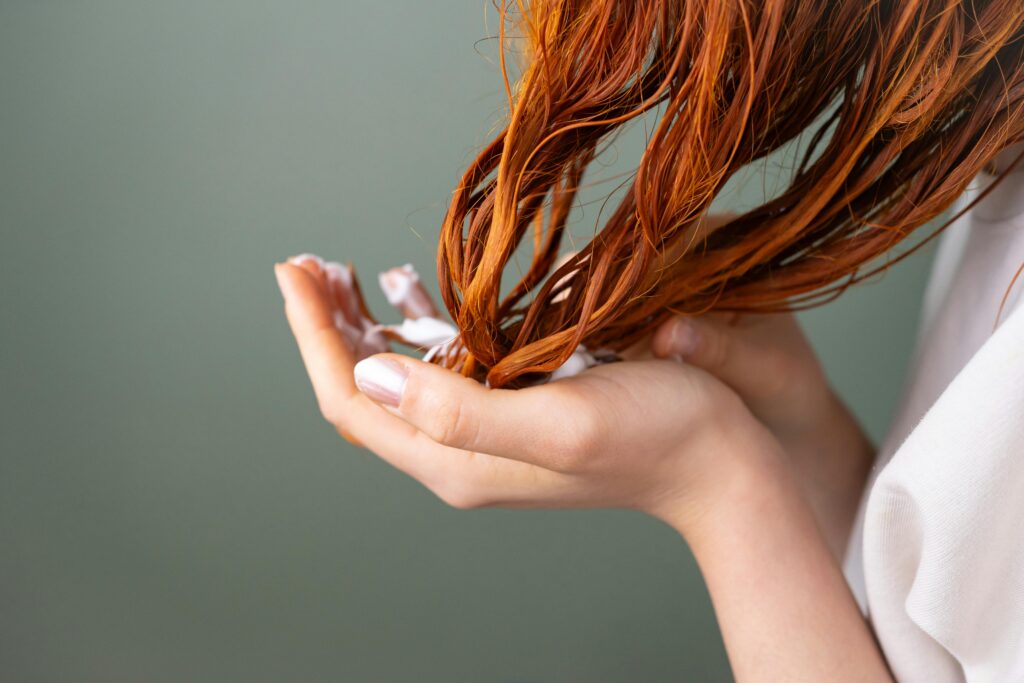 Woman with red hair applying conditioner for healthy hair care.