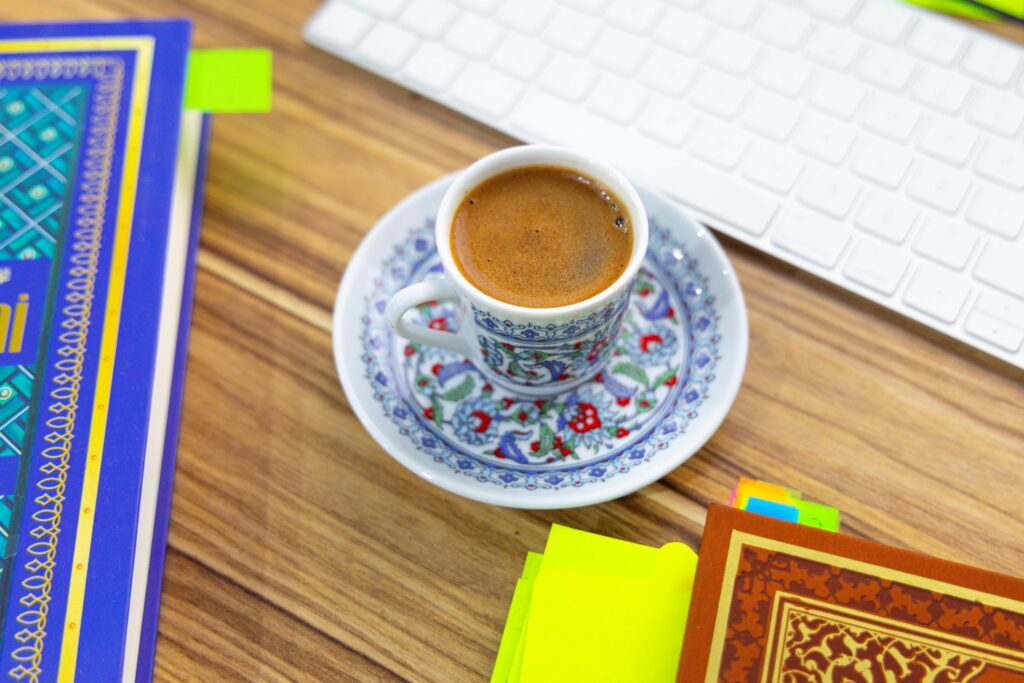 pexels-photo-30674069-30674069 A cup of Turkish coffee sits on a wooden table next to colorful books and a keyboard.