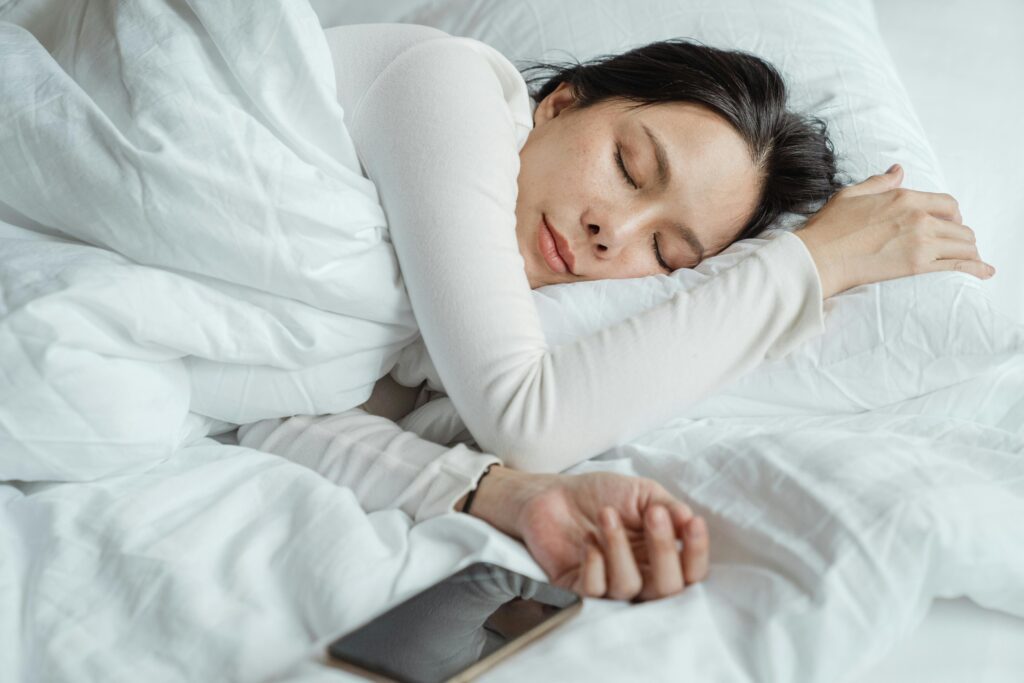 pexels-photo-4473864-4473864 Calm Asian female wearing white pajama sleeping in comfortable bed with white sheets near modern mobile phone in morning