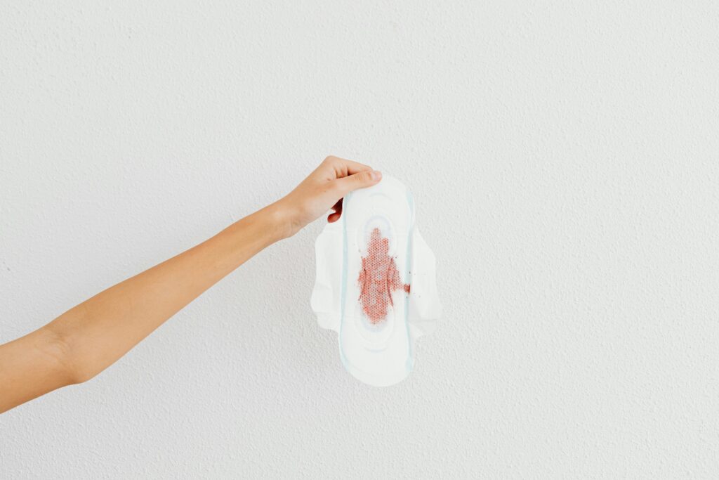 A hand holding a menstrual pad with blood stains, emphasizing menstruation awareness.